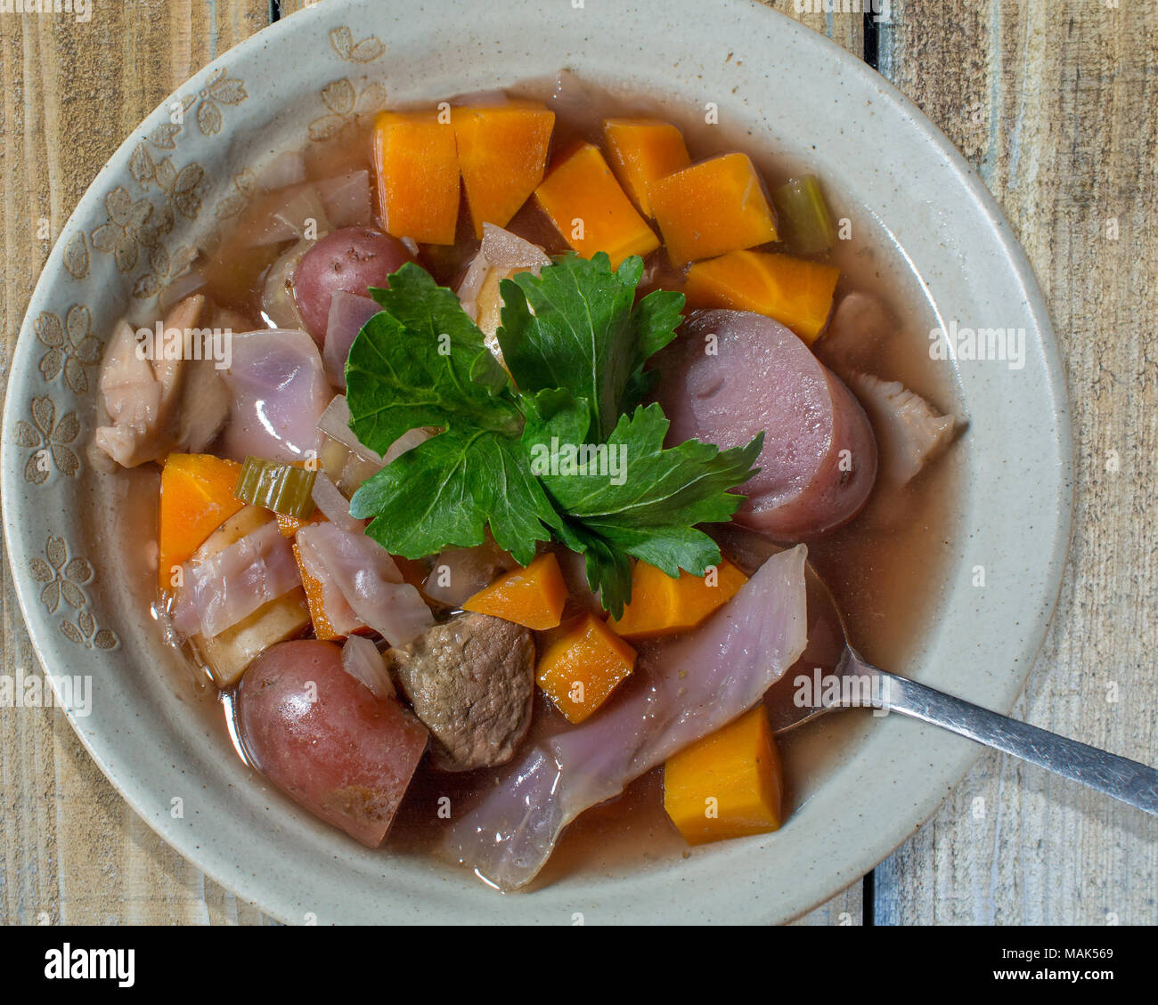 Crockpot Eintopf mit Kartoffeln, Rindfleisch, Rotkraut und Karotten in tan Bogen, garniert mit sellerieblätter, auf Holztisch, gesehen von der Spitze. Stockfoto