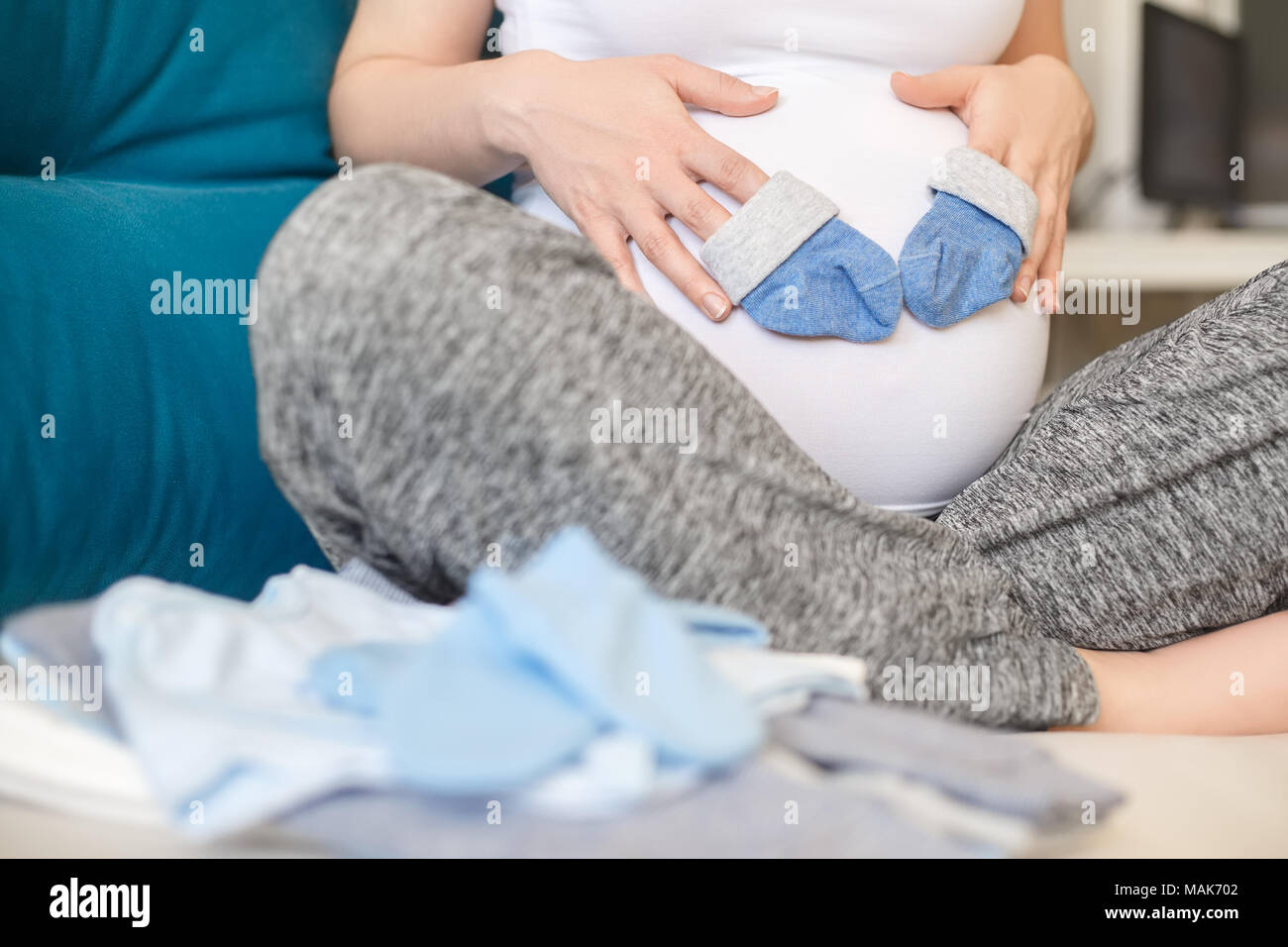 Schwangere Frau mit blauen Socken auf ihren Bauch. Die werdende Mutter vorbereiten Baby Kleidung. Schwangerschaft, Menschen, Erwartung von baby boy Konzept Stockfoto