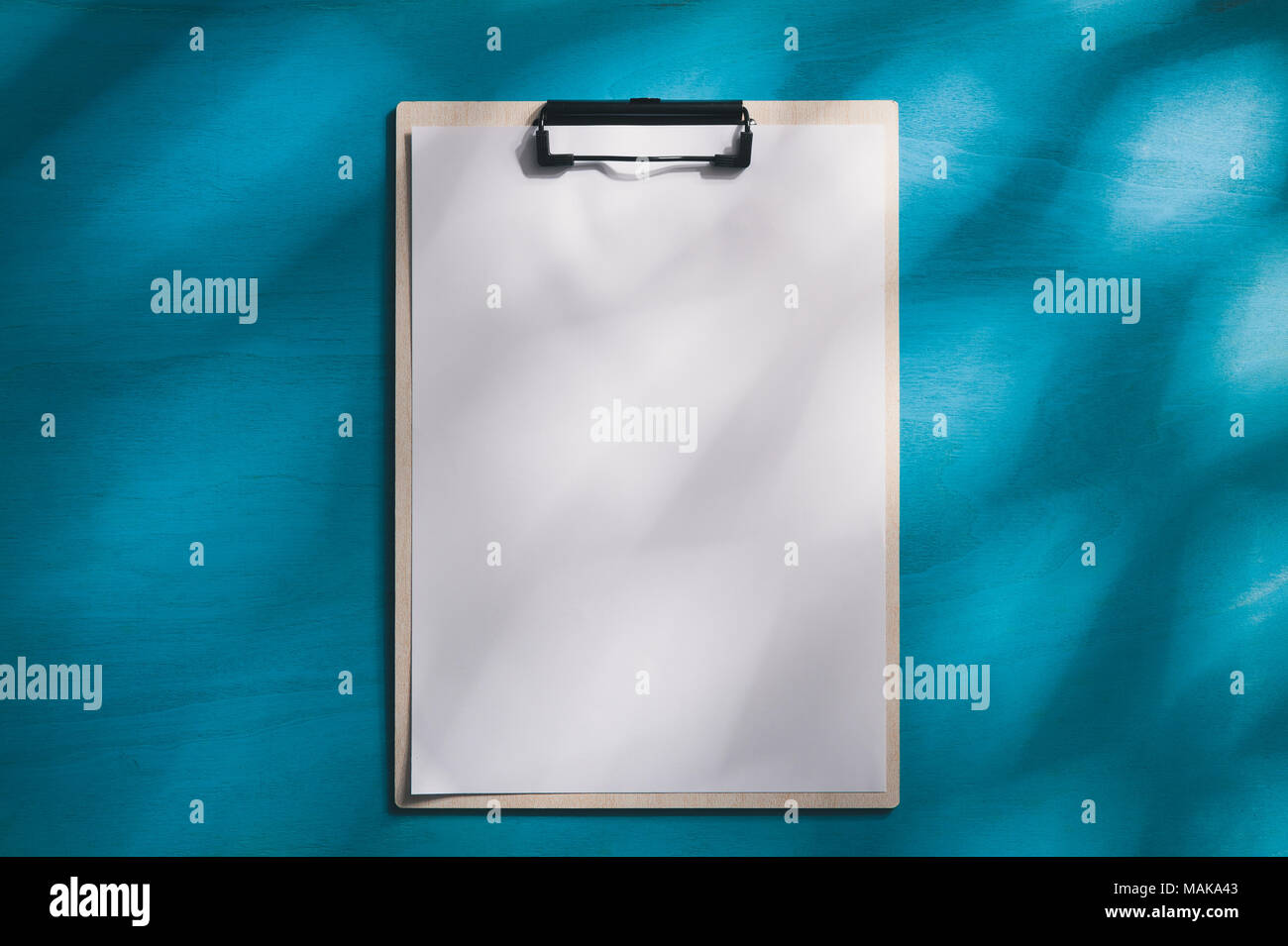 A4-Klemmbrett mit Weißbuch über blau Holz Tisch mit natürlichem Licht am Morgen Zeit. Hintergrund mit leeren Bereich für Text oder Nachricht. Stockfoto