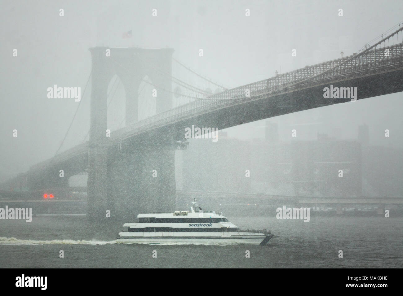 Ein privat eigene SeaStreak Fähre segeln nördlich auf dem East River verläuft unter der Brooklyn Bridge in einem Schneesturm Stockfoto