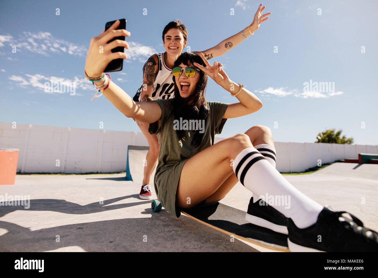 Frau reiten auf Skateboard unter selfie mit Freunden ihn von hinten. Weibliche Freunde eine selfie beim Reiten skateboard Am Skatepark. Stockfoto