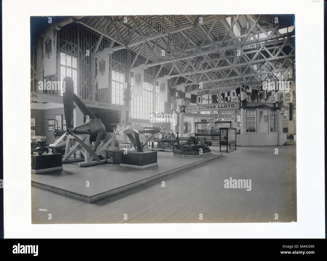 Horizontale schwarze und weiße Foto, das Innere einer Ausstellung Halle mit freiliegenden Dachbalken. Es gibt mehrere grosse Boot Propeller auf der rechten Seite, einige große Schiffsmodelle in Vitrinen auf der rechten Seite der Mitte, und "der Norddeutsche Lloyd" Zeichen in der Anzeige. Banner mit der Darstellung der Deutschen Reichsadler Linie die Wand auf der linken Seite, und eine Reihe von nautischen Wetter Signal flags sind über einem teilweise geschlossenen Ausstellungsflächen in der Ferne auf der rechten Seite hing. Titel: Deutsche Marine Ausstellung im Palast der Transport auf der Weltausstellung 1904. . 1904. Offizielle Photographi Stockfoto