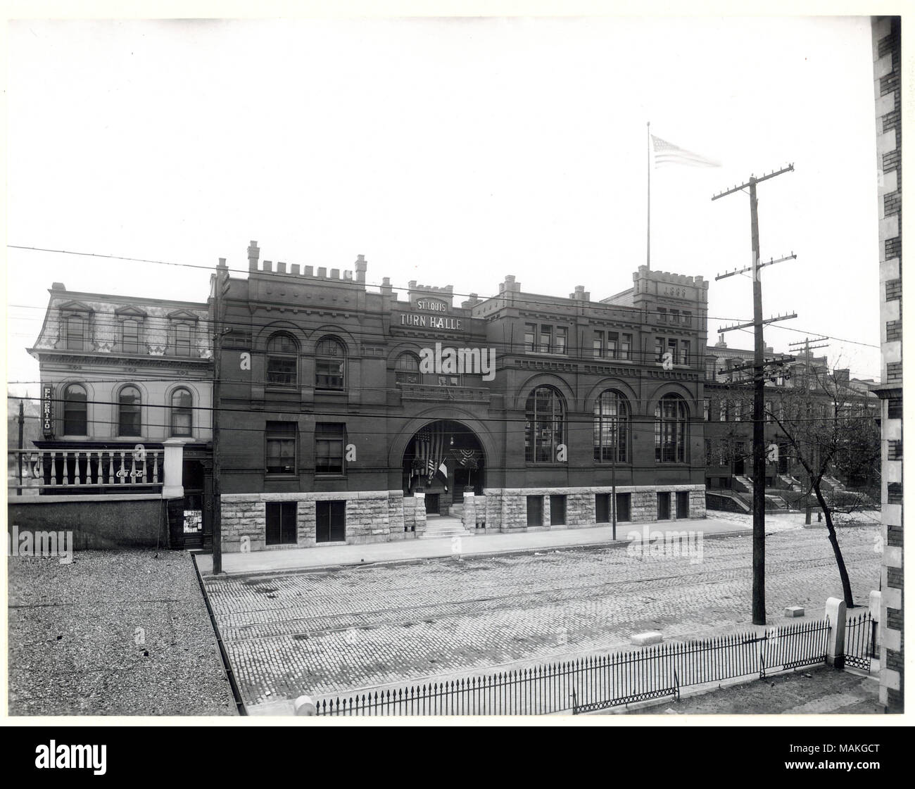 Horizontal, schwarz-weiß Foto eines drei-stöckiges Stein und Ziegel Gebäude aus einer erhöhten Position auf der anderen Seite der Straße. Das Gebäude hat eine gewölbte Eingangshalle mit Fahnen und wimpelketten rund um die Tür. Das Schild über dem Eingang liest 'St. Louis Trun Halle." Titel: St. Louis Turner Hall, 1508 Chouteau Avenue. . Ca. 1900. Oscar C. Kuehn Stockfoto