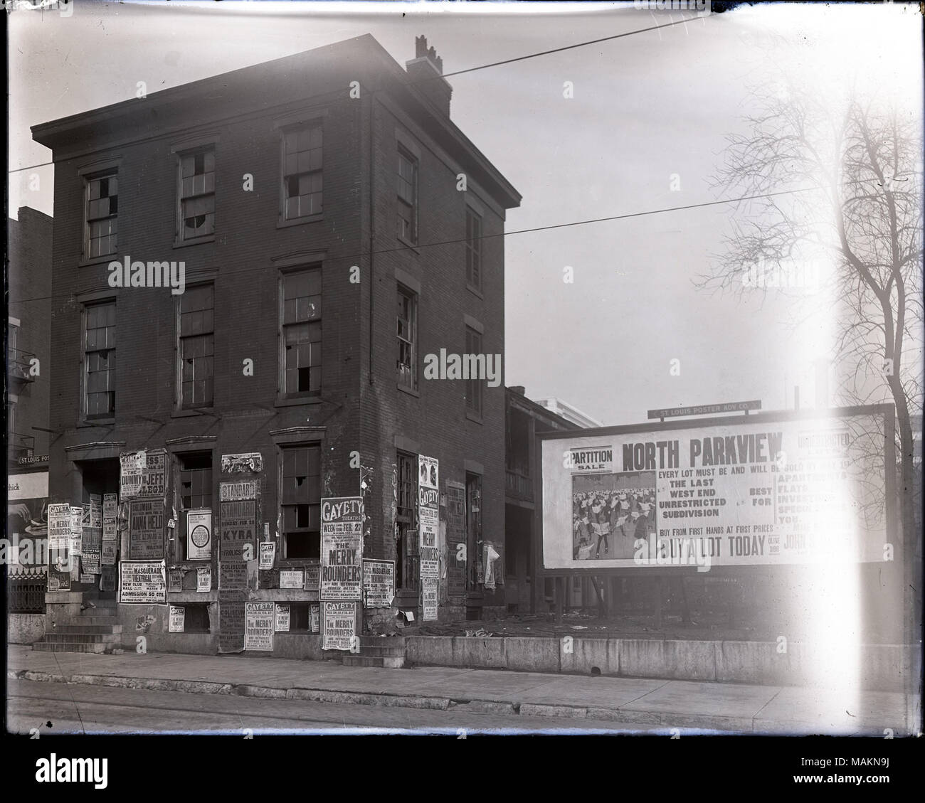 Horizontal, schwarz-weiß Foto zeigt eine verfallene, 3-stöckige Haus mit Plakaten und Anzeigen. Viele der Fenster des Hauses sind gebrochen oder fehlen. Viel von der ersten Geschichte Platz an der Wand ist mit Plakaten und Anzeigen für varieté Produktionen, Zirkusse und andere Veranstaltungen. Auf der rechten Seite, gibt es eine große Werbetafeln Lose zum Verkauf im Norden Parkview Unterteilung im West End. Titel: verfallenen Haus mit Plakaten und Anzeigen. . 1916. Stockfoto