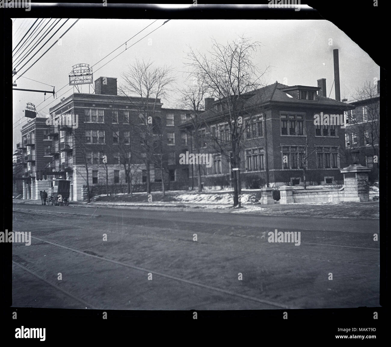Horizontal, schwarz-weiß Foto zeigt zwei Flügel der Harlan Court Apartments Gebäude 5457 Delmar Boulevard und einem benachbarten Haus. Der Blick über die Straße und zeigt die zwei, vier-stöckigen Ziegel und Stein Flügel, mit einem Schild mit der Aufschrift "Harlan Gericht/Elektroherd in jeder Suite' oben auf jedem Flügel. Auf der rechten Seite ist ein Backstein zwei-stöckige Haus mit Bäumen und einem kleinen Hof vor sichtbar. Ein Pferd ziehen eine überdachte Warenkorb kann in der Ferne auf der linken Seite gesehen werden. Titel: Harlan Court Apartments und einem benachbarten Haus 5457 Delmar Boulevard. . Zwischen 1917 und 1918. Stockfoto