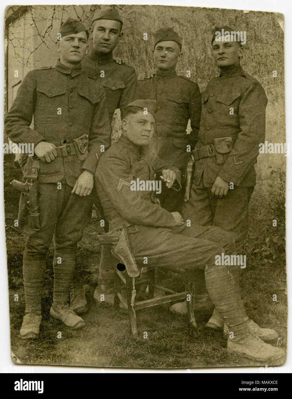 Vertikale, sepia Postkarte mit fünf uniformierte Soldaten für ein Gruppenfoto posieren. Ein Soldat ist auf einem Stuhl sitzen, während die anderen vier Soldaten um ihn herum stehen. Titel: Fünf uniformierte Soldaten für ein Gruppenfoto posieren. . Zwischen ca. 1916 und ca. 1918. Stockfoto