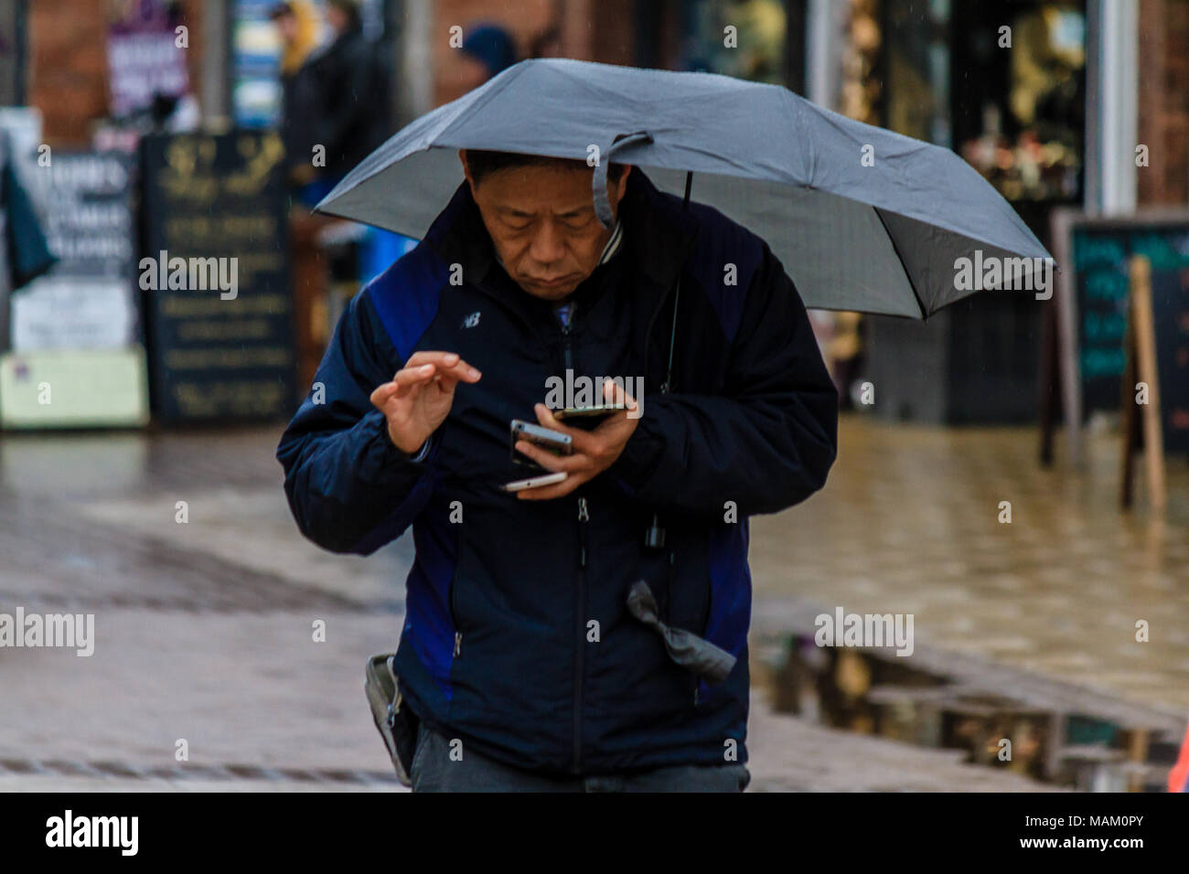 Mann mit Schirm mit Phone im regnerischen Wetter in Stratford-upon-Avon Stadtmitte, England. Stockfoto