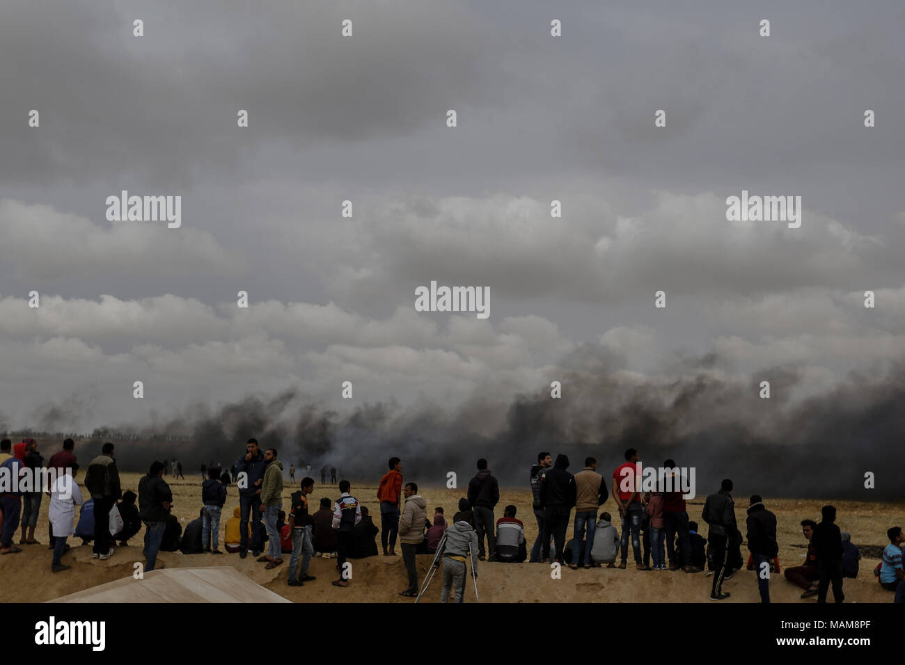 Palästinensische Demonstranten ansehen Rauchwolken, wie sie von verbrannten Reifen steigen, die israelischen Truppen abzulenken, während Auseinandersetzungen entlang der Grenzen zwischen Israel und Gaza, östlich von Khan Yunis, im südlichen Gazastreifen, 03. April 2018. Foto: Mohammed Talatene/dpa Stockfoto