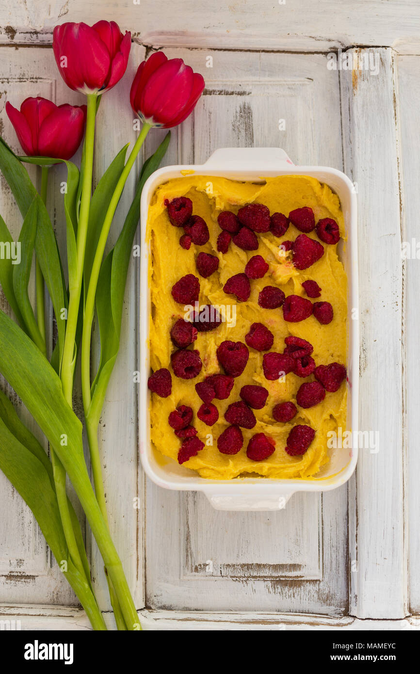 Obere Ansicht geschossen von raw Erdbeertorte in weißen backen Form mit roten Tulpen an seiner Seite weiß, rustikalen Tischplatte Stockfoto