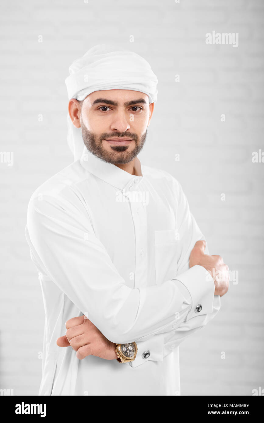 Vertikaler reichen reichen schönen erfolgreichen muslimischen Mann in traditionelle islamische Kleidung posiert in der Nähe von weißen Wand in Photo Studio verwischt. Konzept der Erfolg, cryptocurrency und virtuelles Geld. Stockfoto