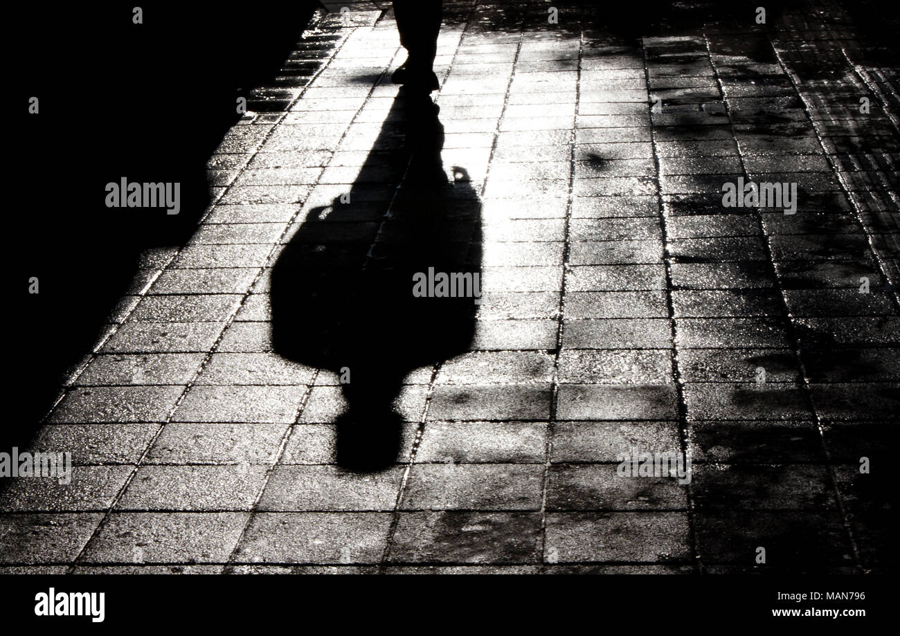 Verschwommene Schatten und Silhouette der Mann in der Nacht auf nasser Straße Bürgersteig mit Wasser Reflexion in Schwarz und Weiß Stockfoto