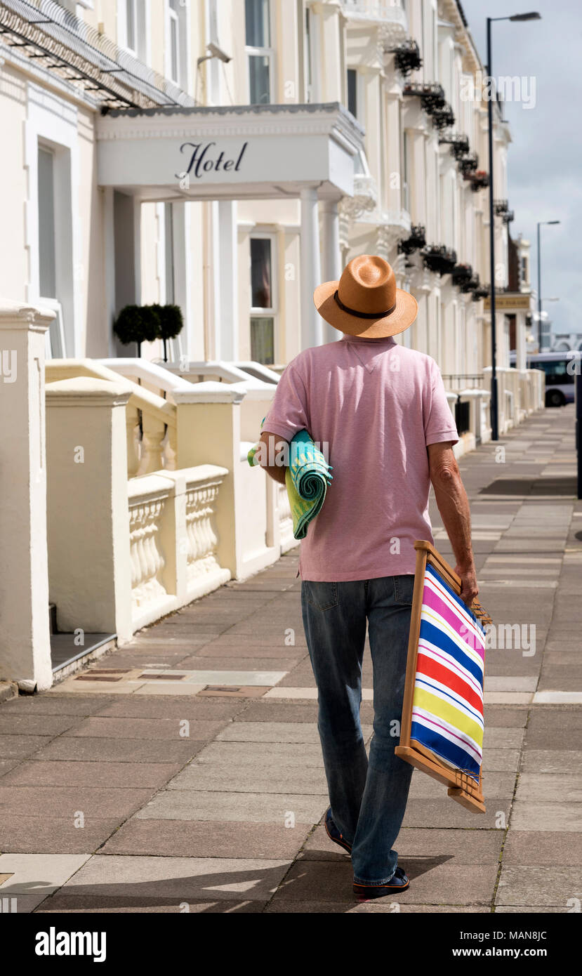 Single Mann allein zu Fuß auf der Suche nach Unterkunft in einem Badeort, ein Liegestuhl und ein Handtuch. Stockfoto