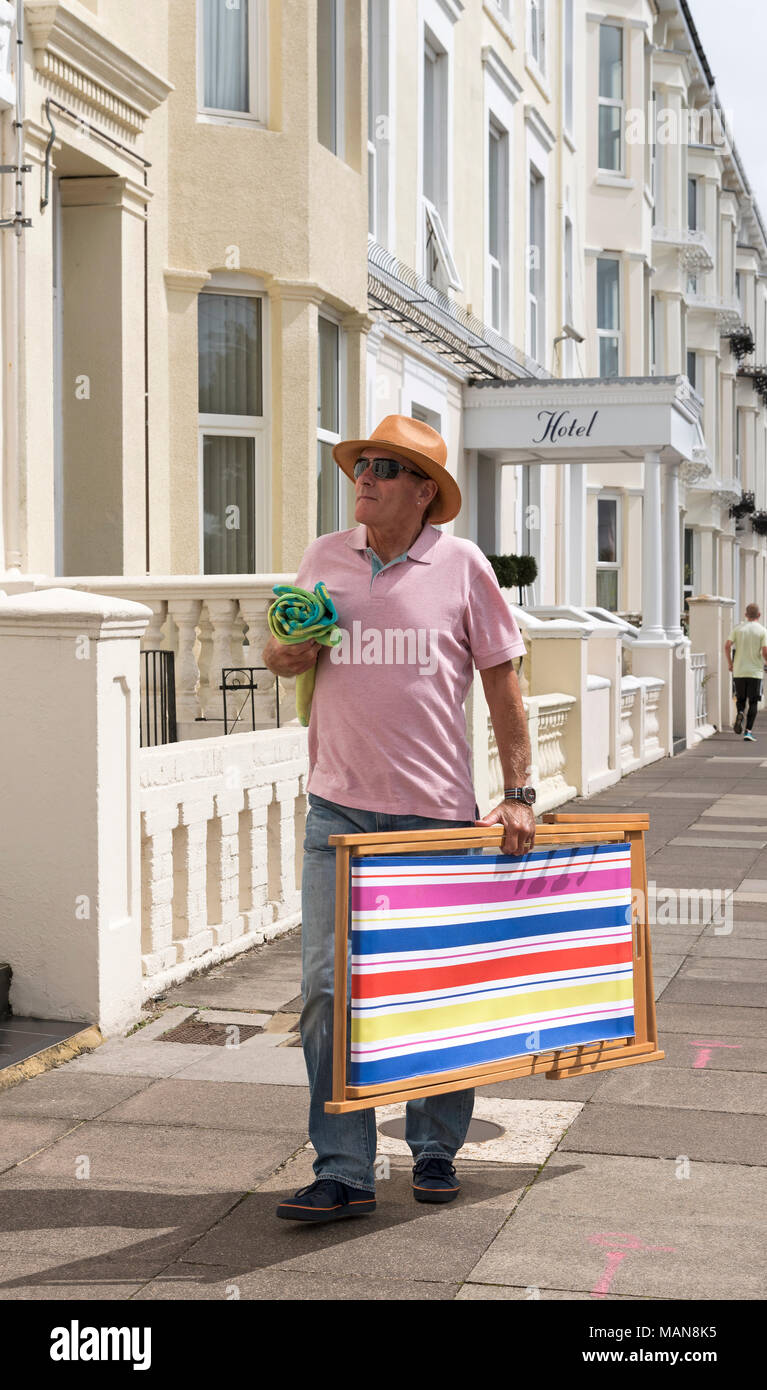 Single Mann allein zu Fuß auf der Suche nach Unterkunft in einem Badeort, ein Liegestuhl und ein Handtuch. Stockfoto