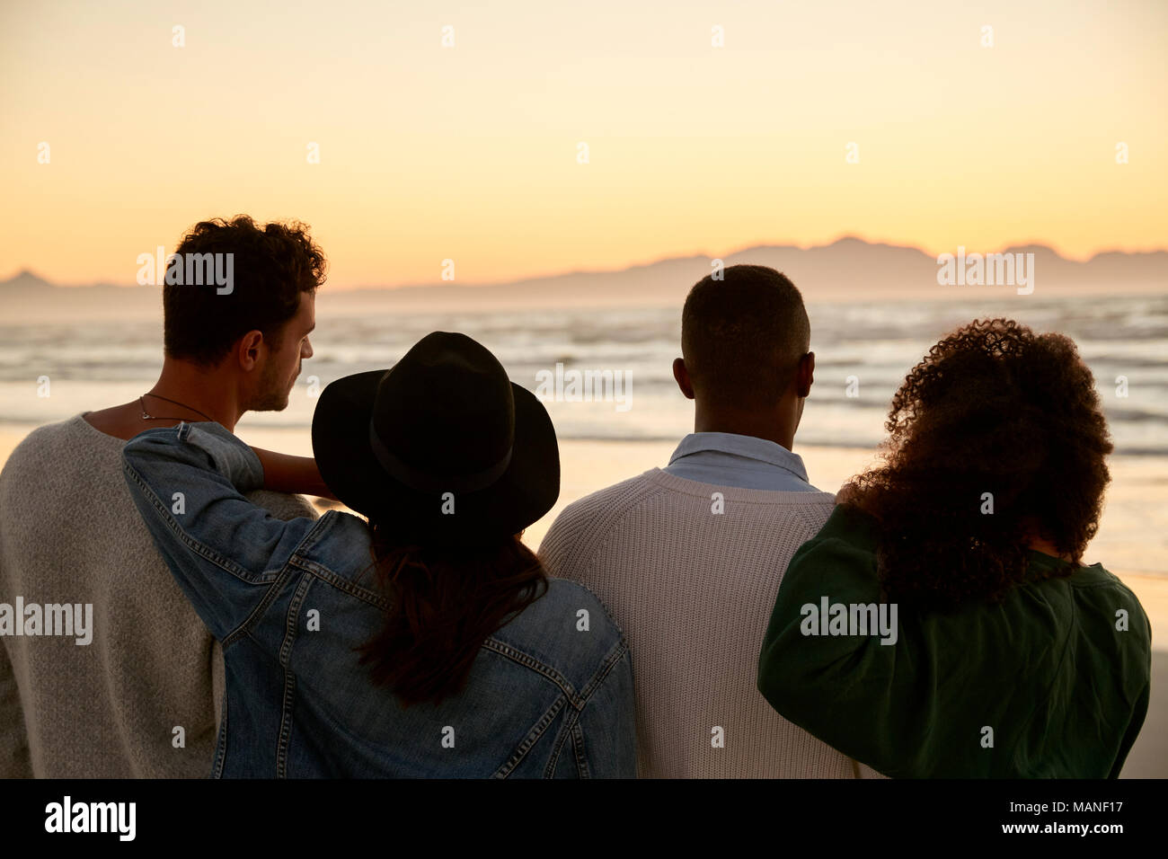 Eine Gruppe von Freunden im Winter Strand beobachten Sonnenaufgang zusammen Stockfoto