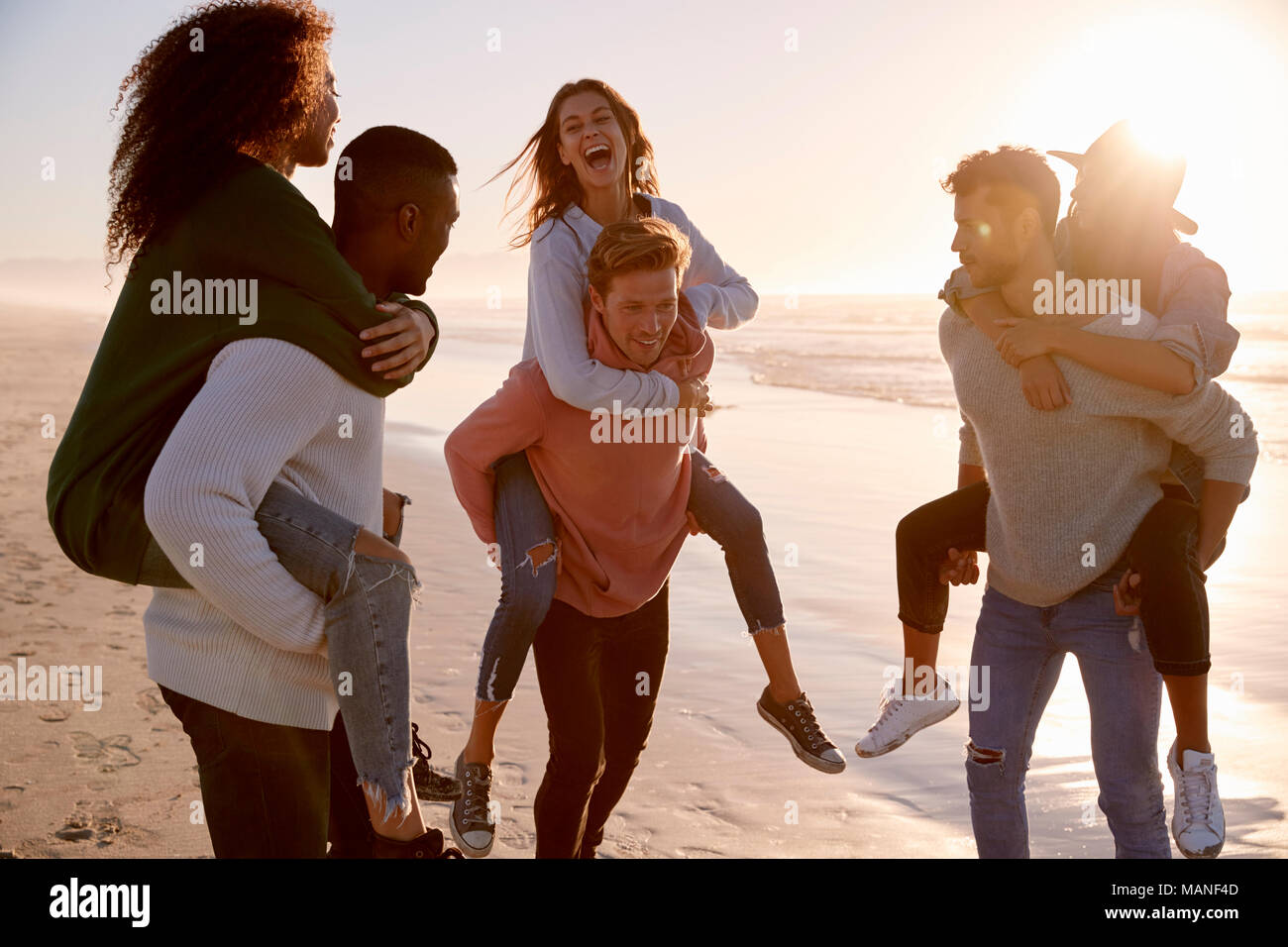 Eine Gruppe von Freunden mit Piggyback Rennen auf Winter Beach zusammen Stockfoto
