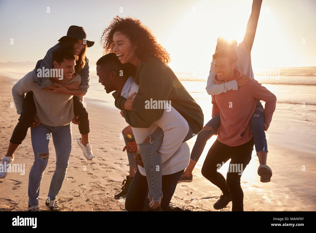 Eine Gruppe von Freunden mit Piggyback Rennen auf Winter Beach zusammen Stockfoto