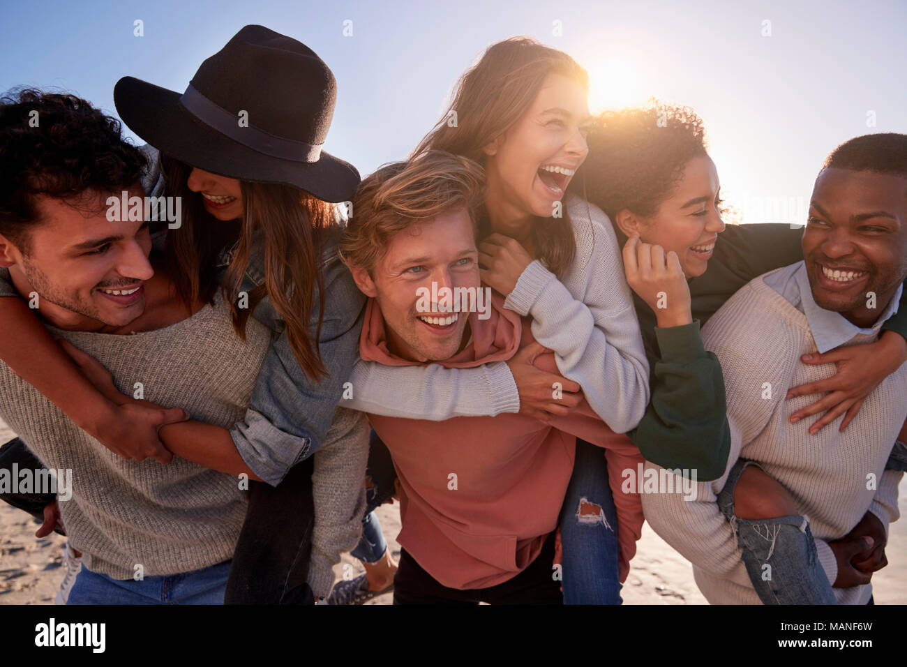 Eine Gruppe von Freunden mit Piggyback Rennen auf Winter Beach zusammen Stockfoto