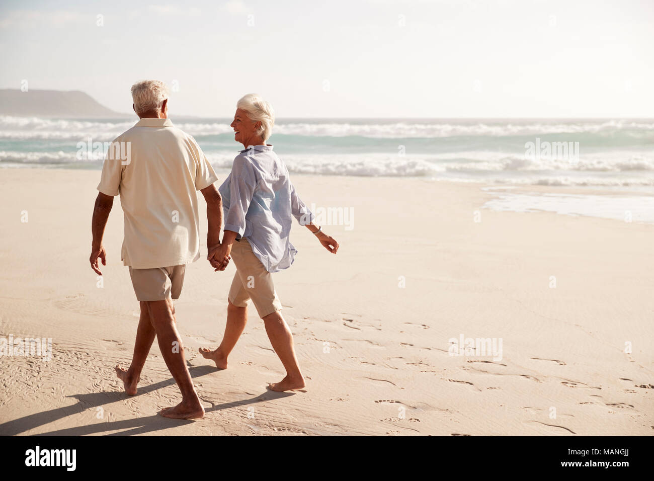 Ansicht der Rückseite des Senior Paar am Strand entlang zu laufen Hand in Hand Stockfoto