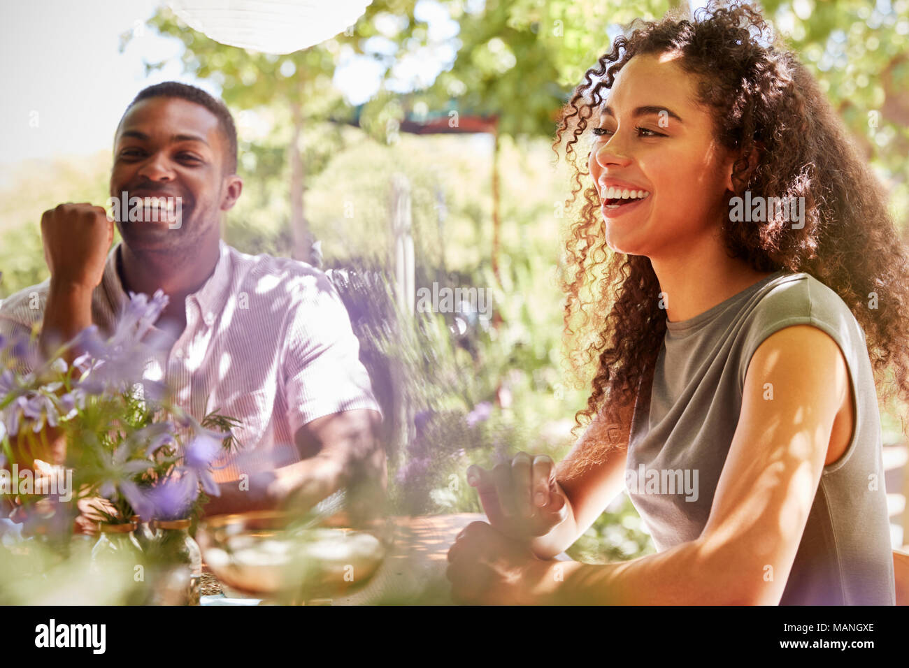 Junge Erwachsene Freunde an einem Tisch sitzen in einem Garten lachen Stockfoto