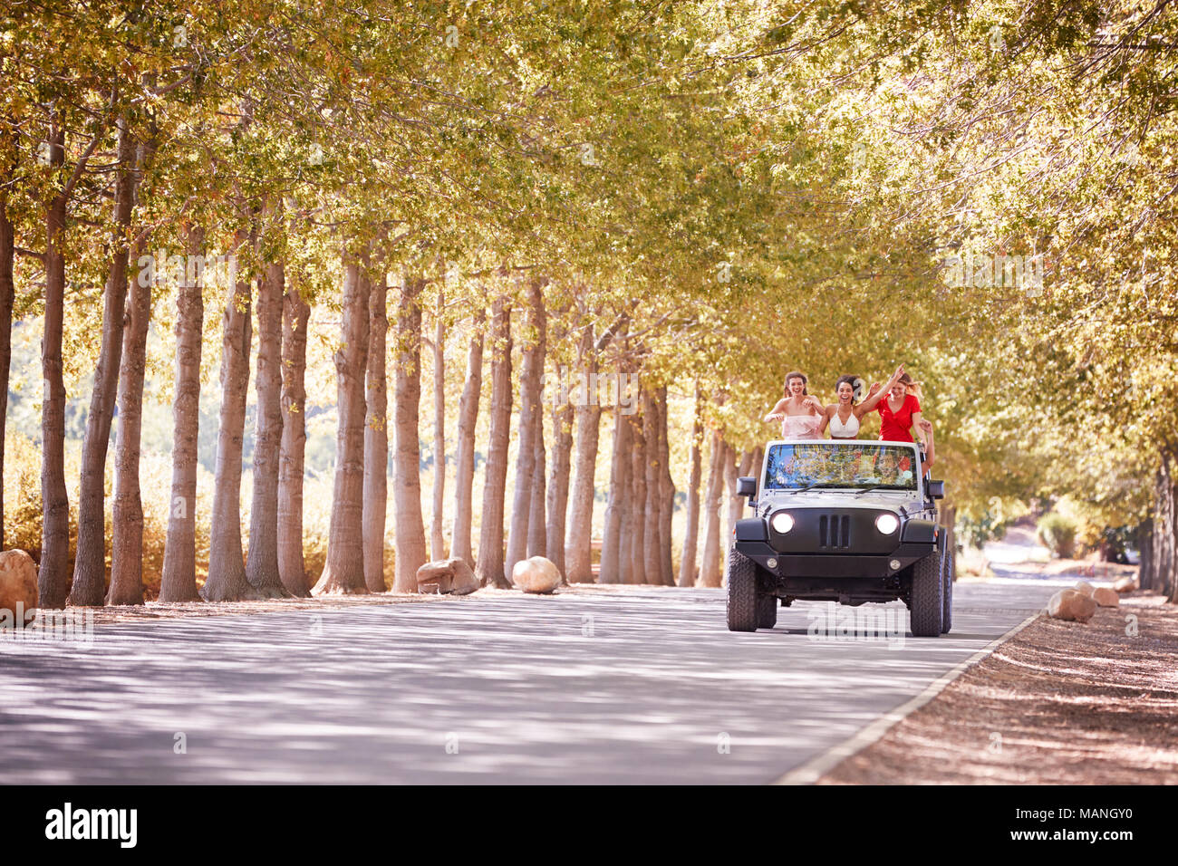 Freunde fahren auf eine leere Straße in einem oben offenen Jeep Stockfoto