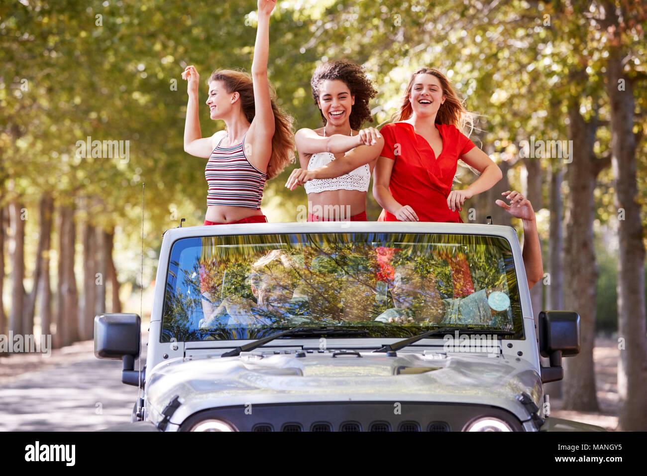 Freundinnen in einem oben offenen Auto stehend mit den Armen in der Luft Stockfoto