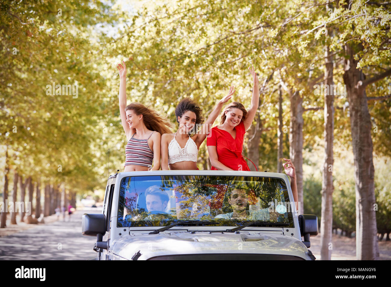 Freundinnen in der Rückseite eines oben offenen Auto stehend winken Stockfoto