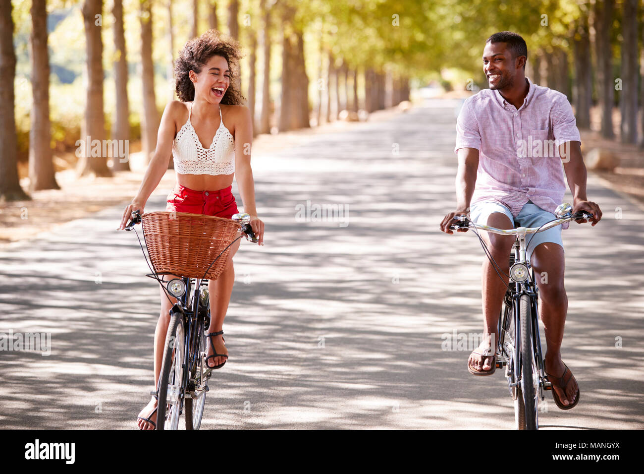 Lachen junges Paar auf dem Fahrrad über eine sonnige Straße Stockfoto