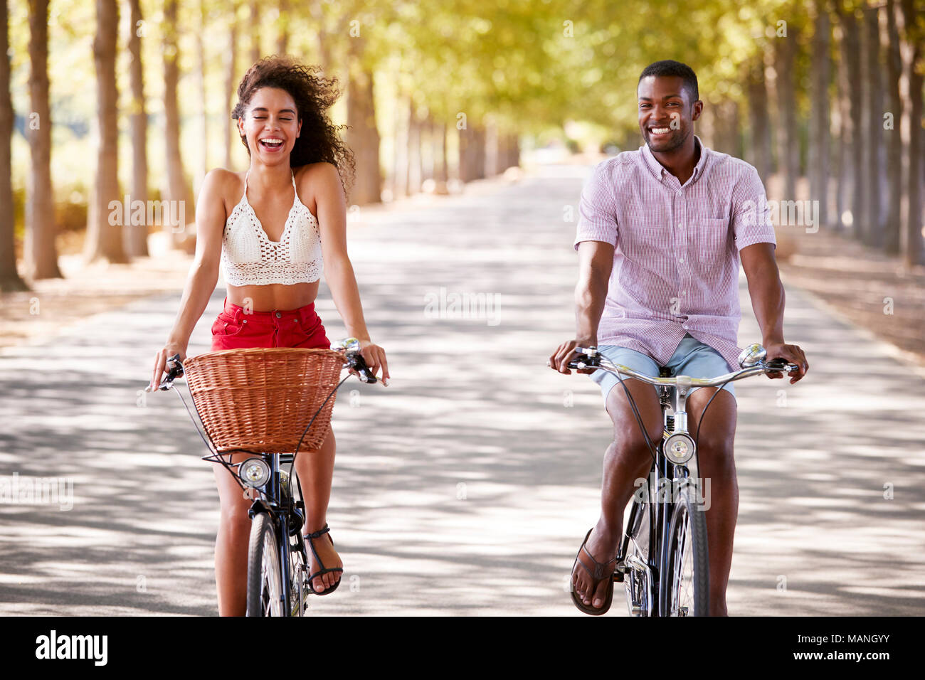 Junge Mixed Race Paar Fahrrad auf einer von Bäumen gesäumten Straße Stockfoto