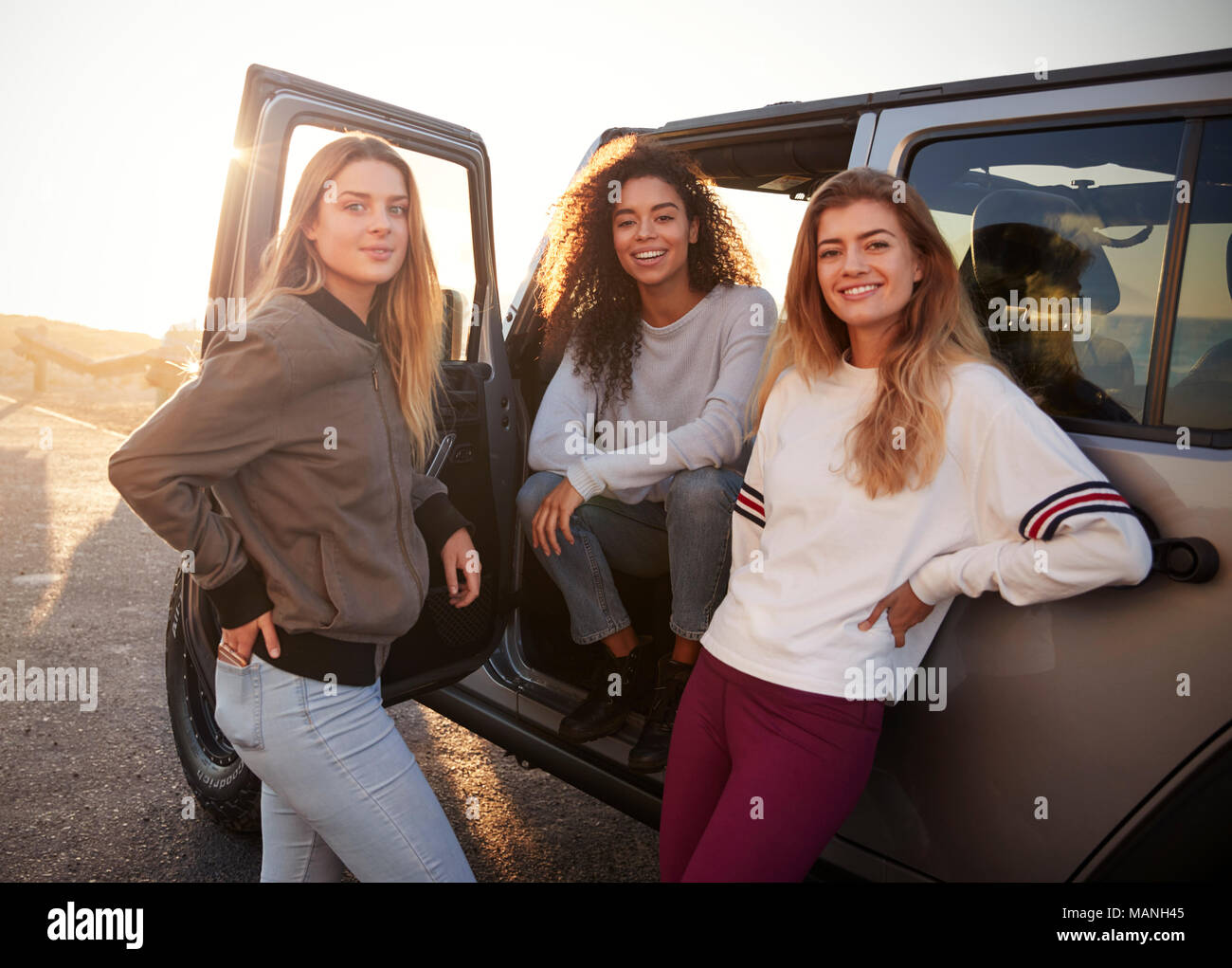 Drei weibliche Freunde auf der Straße Reise in die Kamera schaut vom Auto Stockfoto