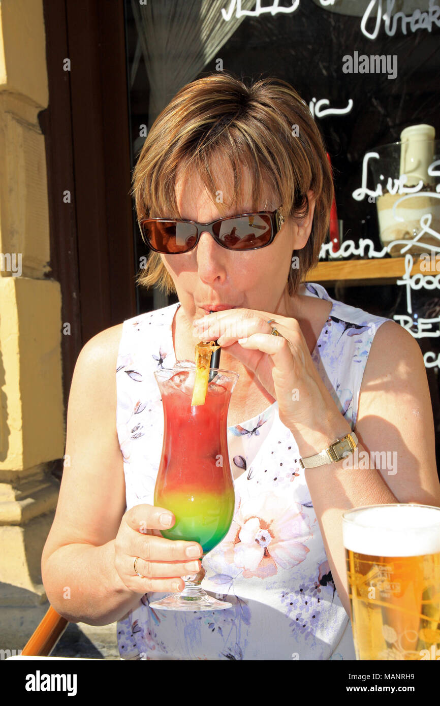 Frau/Dame sitzen draußen in der Sonne in einem Cafe Bar mit einem bunten Cocktail Trinken durch einen Halm in der Stadt Budapest Ungarn Stockfoto