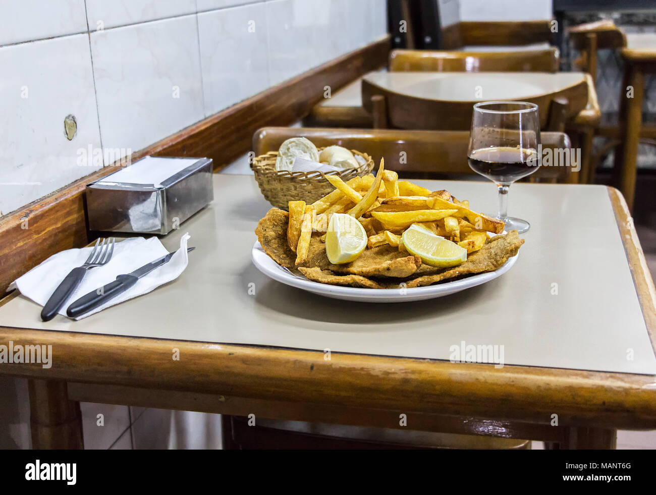 Eine Platte mit Milanesas con Papas fritas (Schnitzel mit Kuh Rind und Pommes frites Kartoffeln gemacht) auf einem hölzernen Tisch in einem kleinen Restaurant für Arbeitnehmer in Buenos Stockfoto