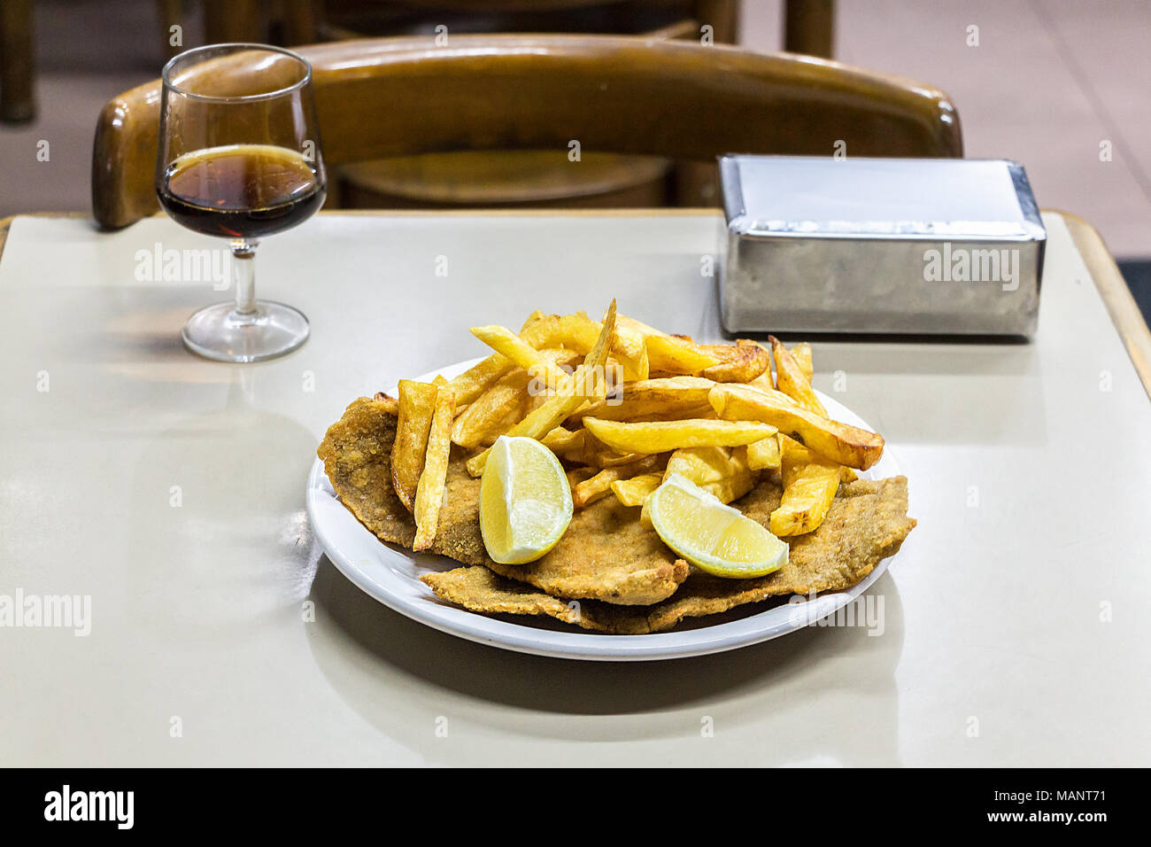 Eine Platte mit Milanesas con Papas fritas (Schnitzel mit Kuh Rind und Pommes frites Kartoffeln gemacht) auf einem hölzernen Tisch in einem kleinen Restaurant für Arbeitnehmer in Buenos Stockfoto