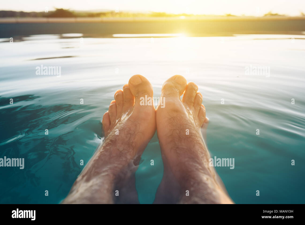 Männliche Füße im Außenpool. Mann genießen Sie erfrischende Pool Wasser im Sommer Sonnenuntergang. Ferien und Wochenende. Stockfoto