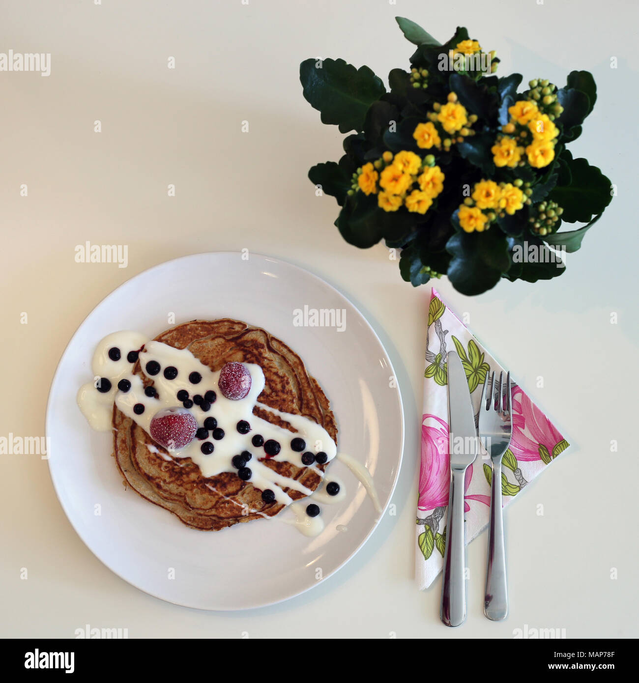 Eine Platte der hausgemachte Pfannkuchen mit Joghurt und Beeren serviert. Es gibt auch Geschirr und schöne gelbe Blume im Bild. Stockfoto