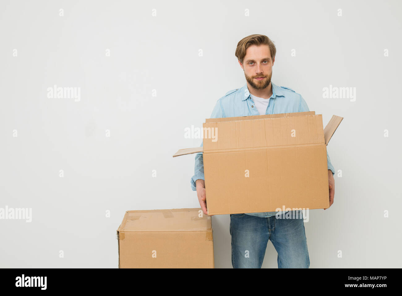 Ein junger blonder Mann, tragen einige Kartons, Delivery Man, oder ein Kerl, der die Dinge in ein anderes Heim bewegt sich auf einem weißen Hintergrund, Kamera suchen Stockfoto