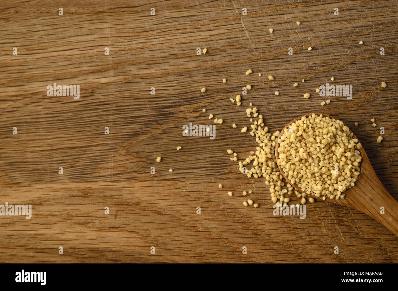 Overhead shot der Löffel aus Holz, mit rohen couscous Getreide gefüllt, auf den alten, verkratzten Eiche Oberfläche. Stockfoto