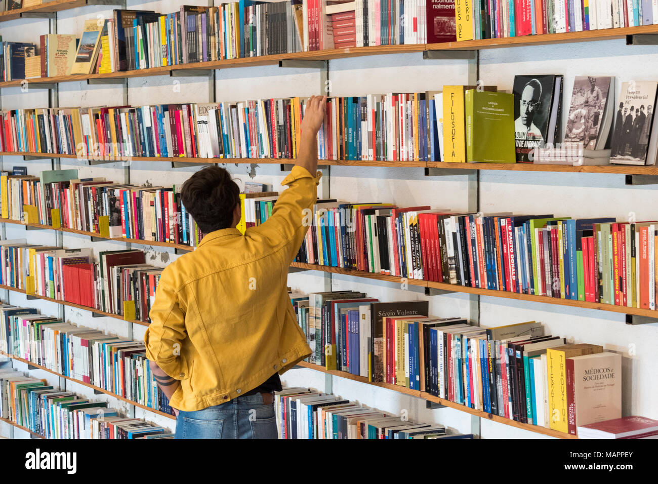 Junger Mann in einer gelben Jacke Auswahl Bücher bei Ler Devagar Buch Shop im LxFactory, Lissabon, Portugal Stockfoto