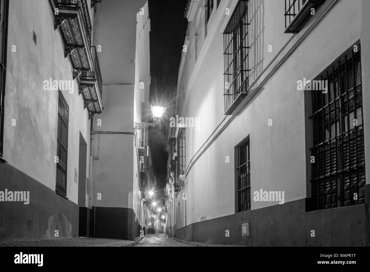 Monochrome eines Night Street Scene/Blick auf eine schmale Straße mit Kopfsteinpflaster im Barrio/Bezirk Santa Cruz in Sevilla 2018, Andalusien, Spanien Stockfoto