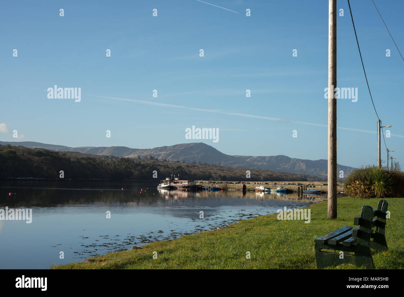 Einsame Bank und festgemachte Boote und Yachten in Kenmare Bay, County Kerry, Irland. Sonniges irisches Wetter. Idyllischer Morgen am Meer. Stockfoto