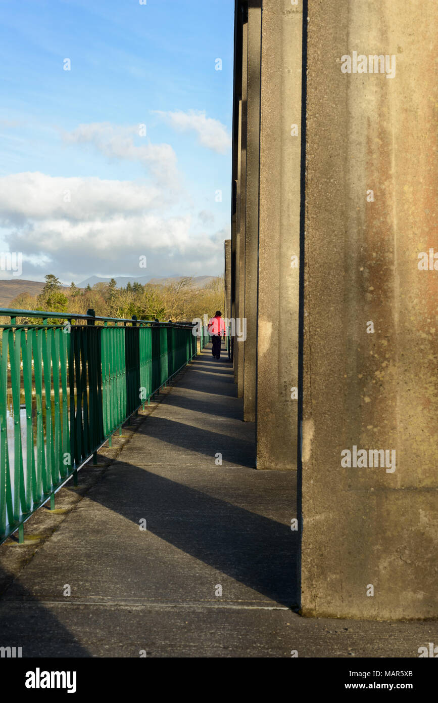 Einsame Person in roter Jacke, die auf der Hängebrücke, The Sound, Kenmare, Irland läuft. Stockfoto