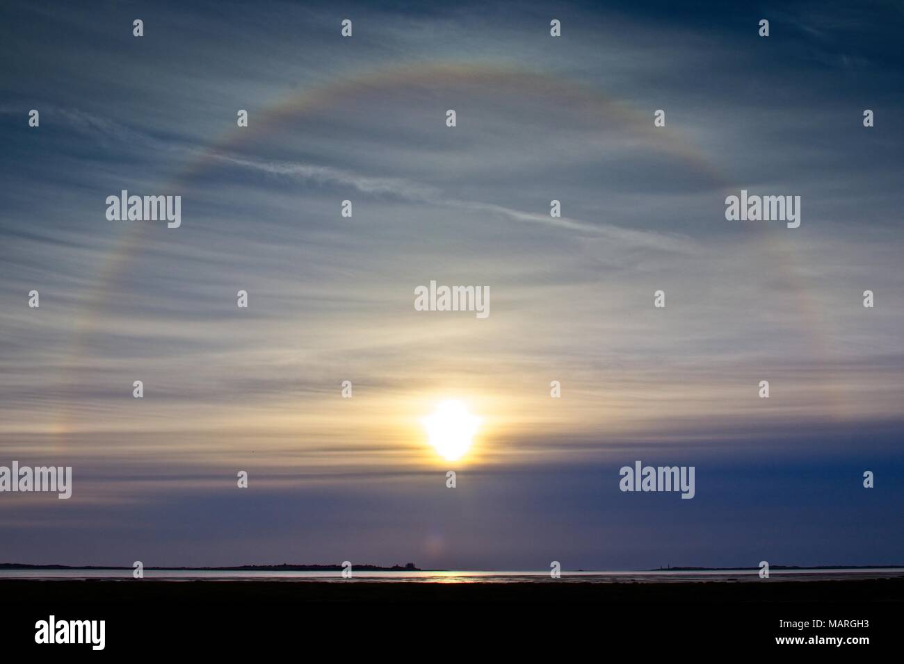 Ein Blick über das Meer in Richtung Lindisfarne mit einem solar Halo um die Sonne bei Sonnenaufgang nach Osten. Stockfoto