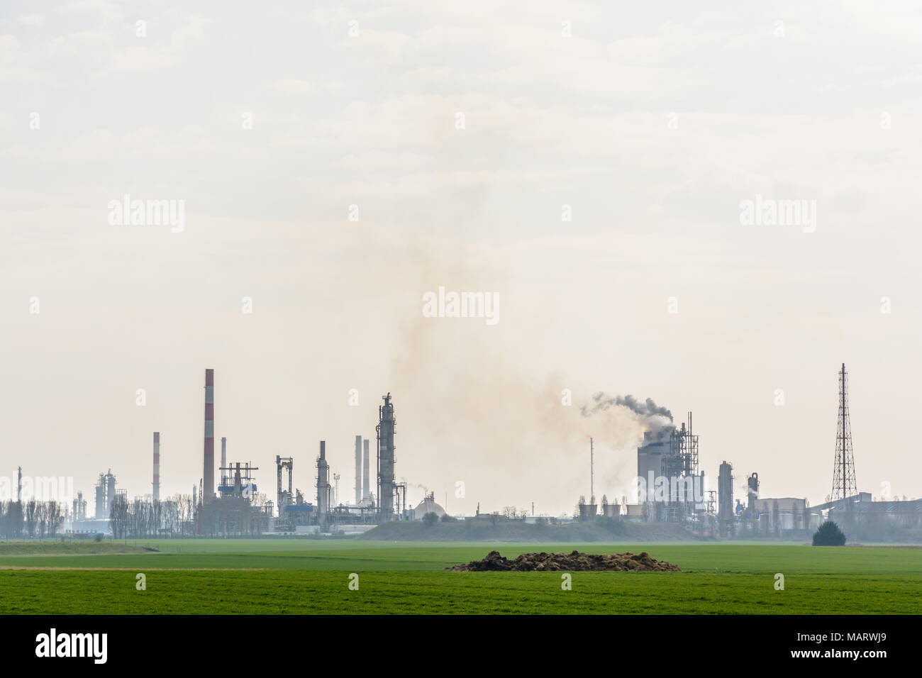 Eine Ölraffinerie mit rauchenden Schornsteine Freisetzung toxischer Gase in der Luft, von Getreidefelder in der französischen Landschaft unter einem hellen Sonnenlicht umgeben. Stockfoto