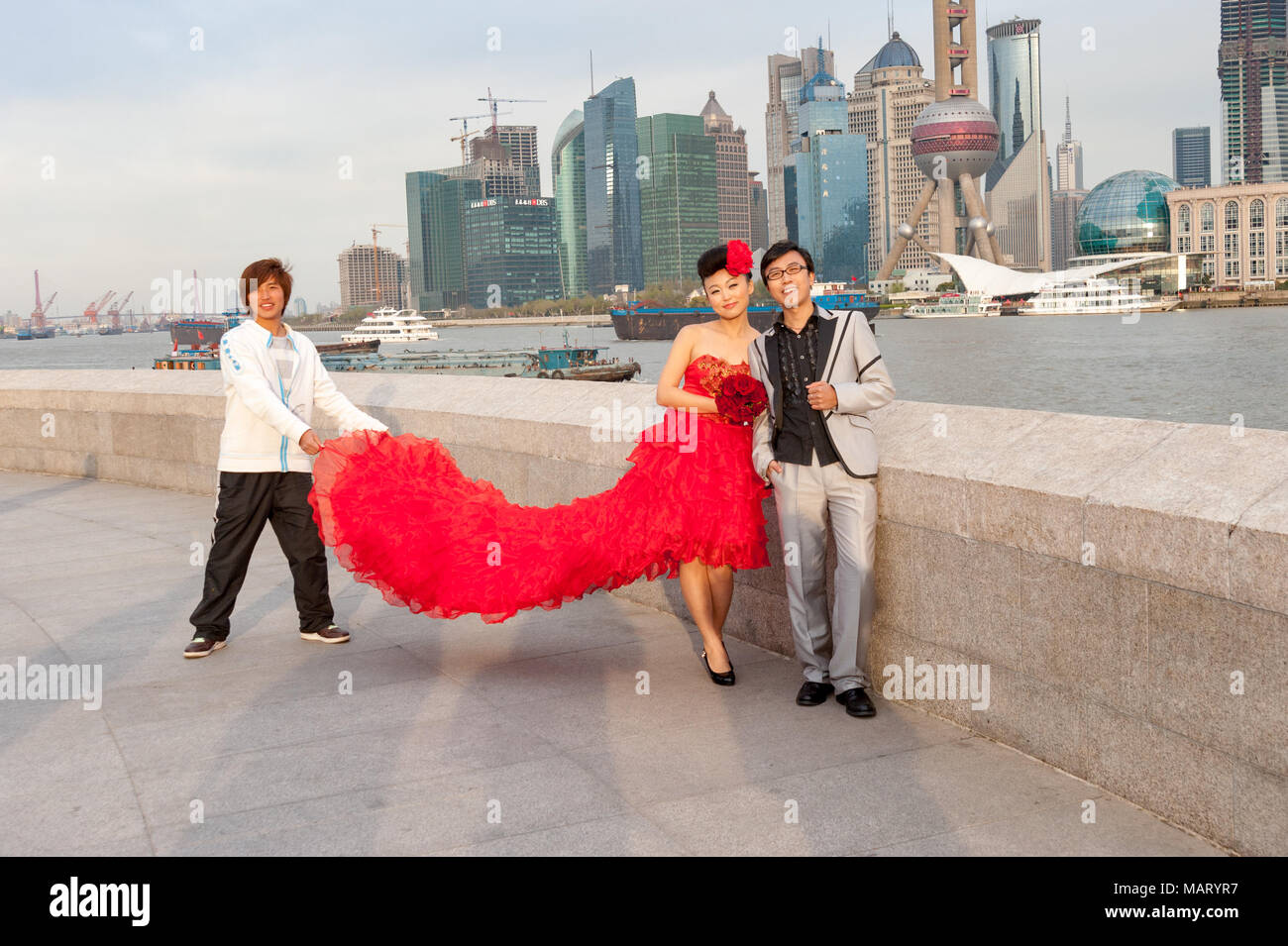 Junge frisch vermählte Paar mit Fotos, auf den Bund gegen die Skyline der Stadt Shanghai, China Stockfoto