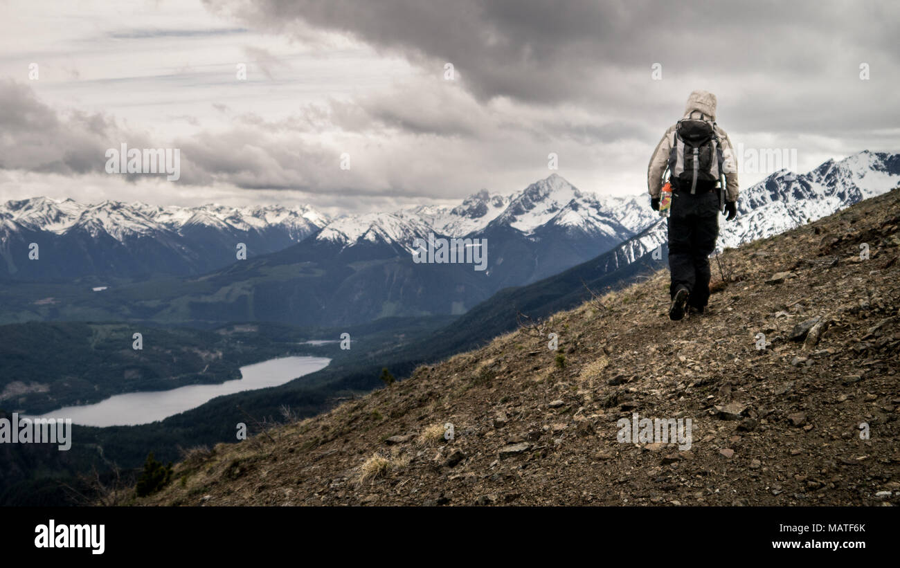 Wanderer entlang eine Geröll Ridge im frühen Frühling. Die schneebedeckten Berge und Gun See in der Ferne (Gold Bridge, BC, Kanada) Stockfoto