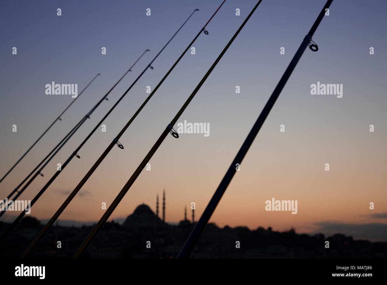 Eine Reihe von Angelruten und fernen Moschee bei Sonnenuntergang von der Galatabrücke in Istanbul, Türkei. Stockfoto