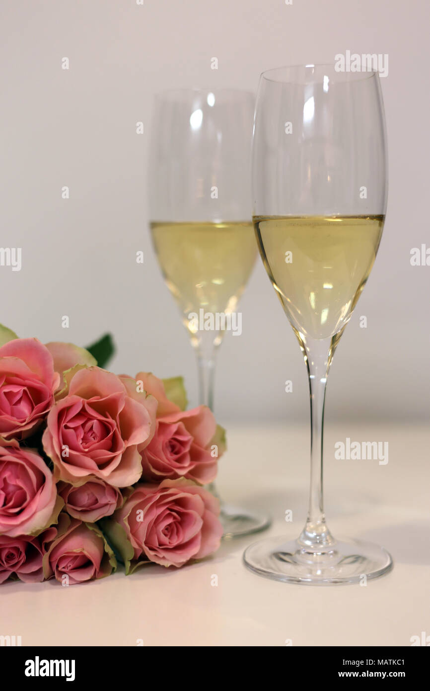 Zwei Champagnergläser/Sekt Gläser auf einem weißen Tisch ist mit einem Strauß aus Rosen fotografiert. Luxuriöse Feier! Stockfoto