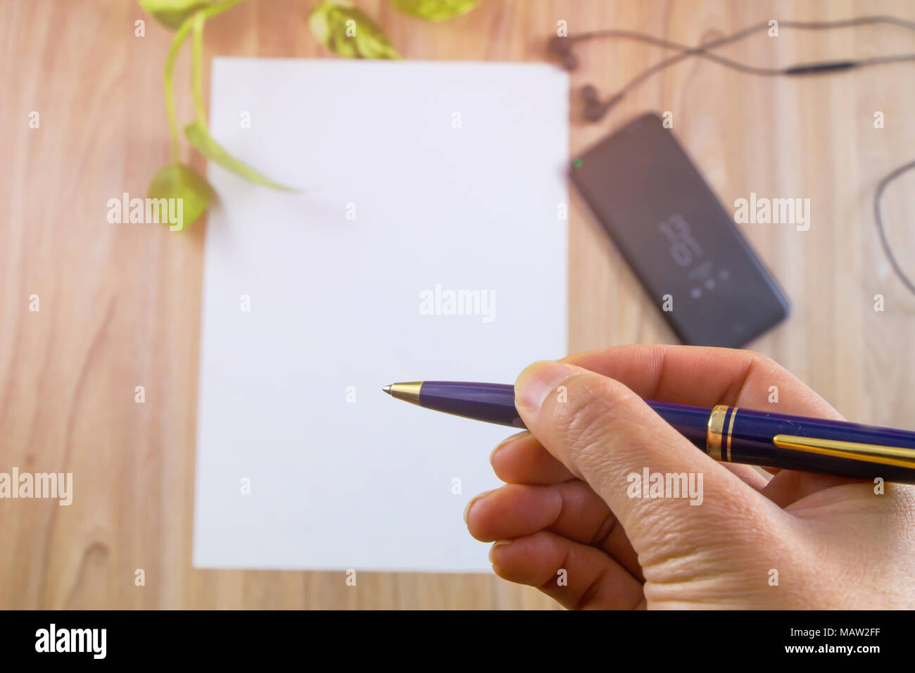 Selektiver Fokus, Hand mit einem Stift auf weißem Papier und modernen Smartphone auf Holztisch, Ansicht von oben mit der Kopie schreiben, unscharfer Hintergrund. Stockfoto