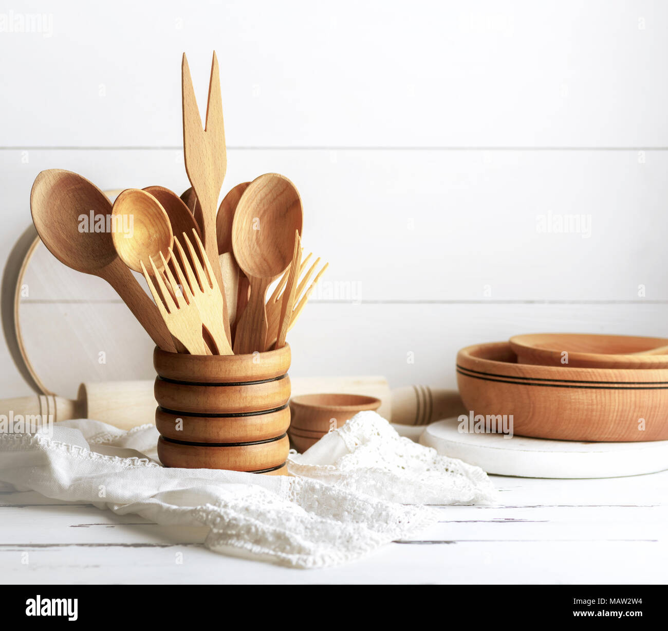 Verschiedene Gegenstände aus Holz in einem hölzernen Becher, Löffel, Gabeln, Nudelholz, Teller und ein Sieb auf einem weißen Tisch Stockfoto