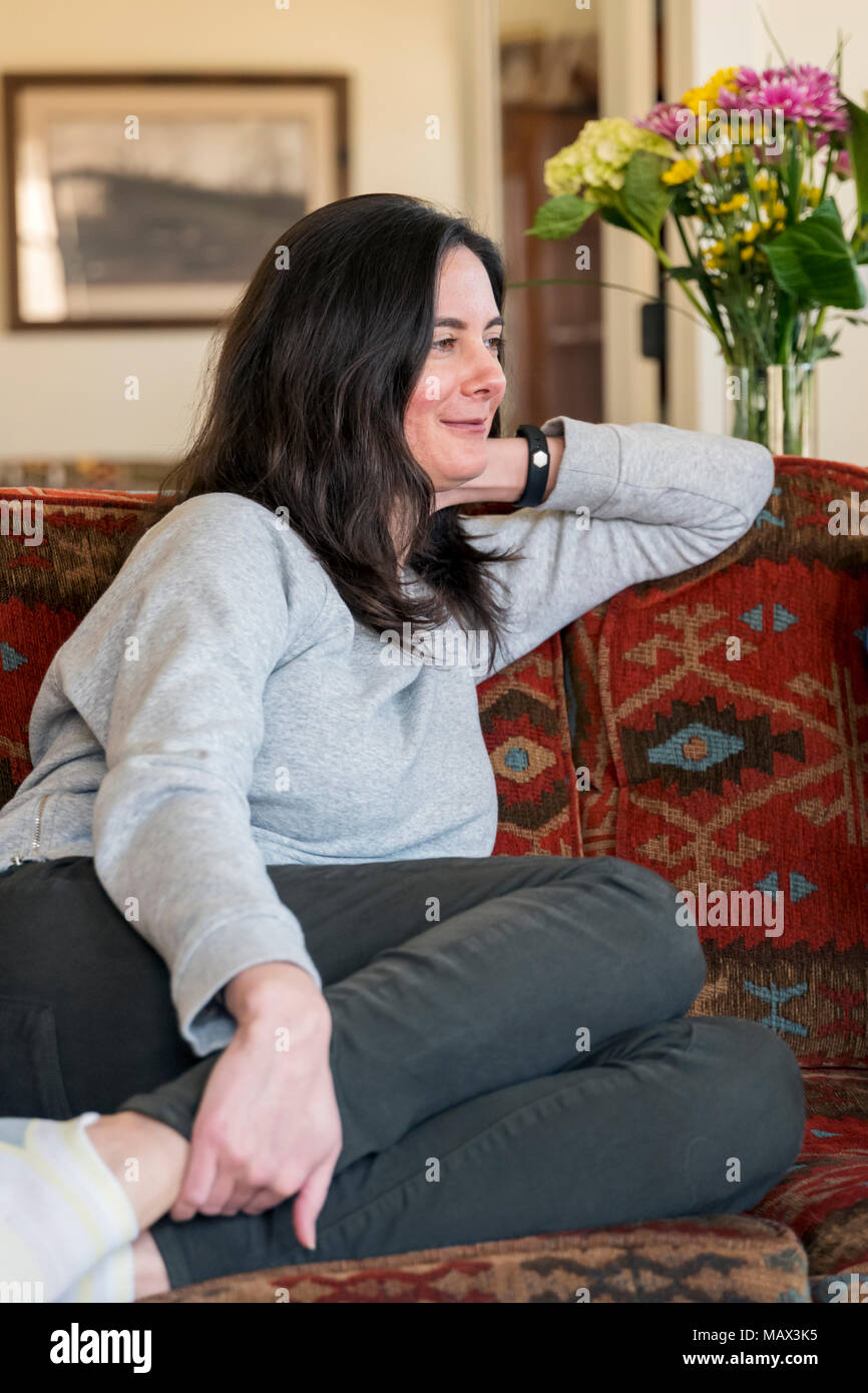 Frau beiläufig auf Sofa im Wohnzimmer sitzen Stockfoto