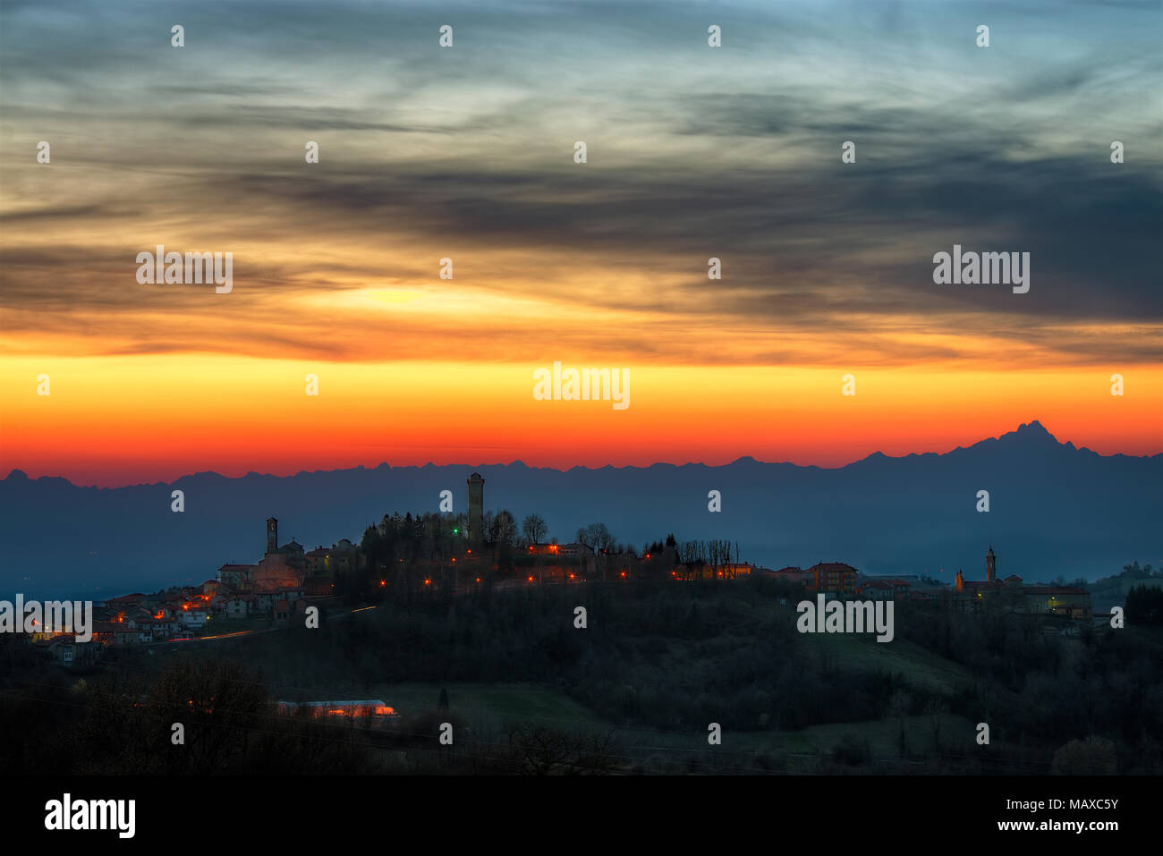 Langhe - eine brennende Himmel, bei Einbruch der Dunkelheit, zeichnet die Skyline der Alpen, mit den hohen Monviso, während in der Stadt von murazzano der Leuchten. Stockfoto